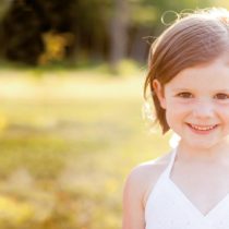 Ein Kind mit weißem Kleid und Blume im Haar lächelt in die Kamera