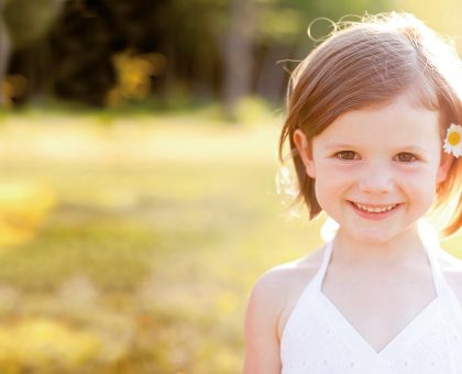 Ein Kind mit weißem Kleid und Blume im Haar lächelt in die Kamera