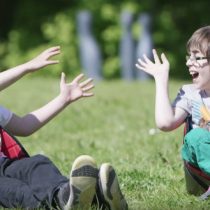 Zwei kleine behinderte Kinder sitzen in einer Sitzhilfe uns werden sich den Ball zu