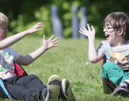 Zwei kleine behinderte Kinder sitzen in einer Sitzhilfe uns werden sich den Ball zu