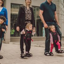 3 Elternteile mit ihren kleinen Kindern, die beim Gehen Unterstützung bekommen