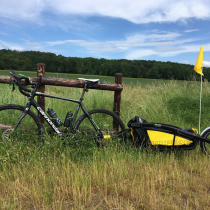 Stefan Welbs Fahrrad mit Anhänger auf der grünen Wiese an einm Holzzaun angelehnt.