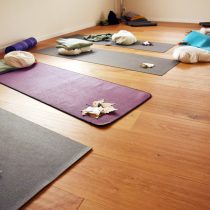 Yogamatten auf dem Holzdielenboden mit Kissen und Herbstblättern.