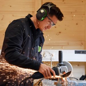 Ein Orthopädietechniker schleift in der Werkstatt und hat Schallschutz-Kopfhörer auf.