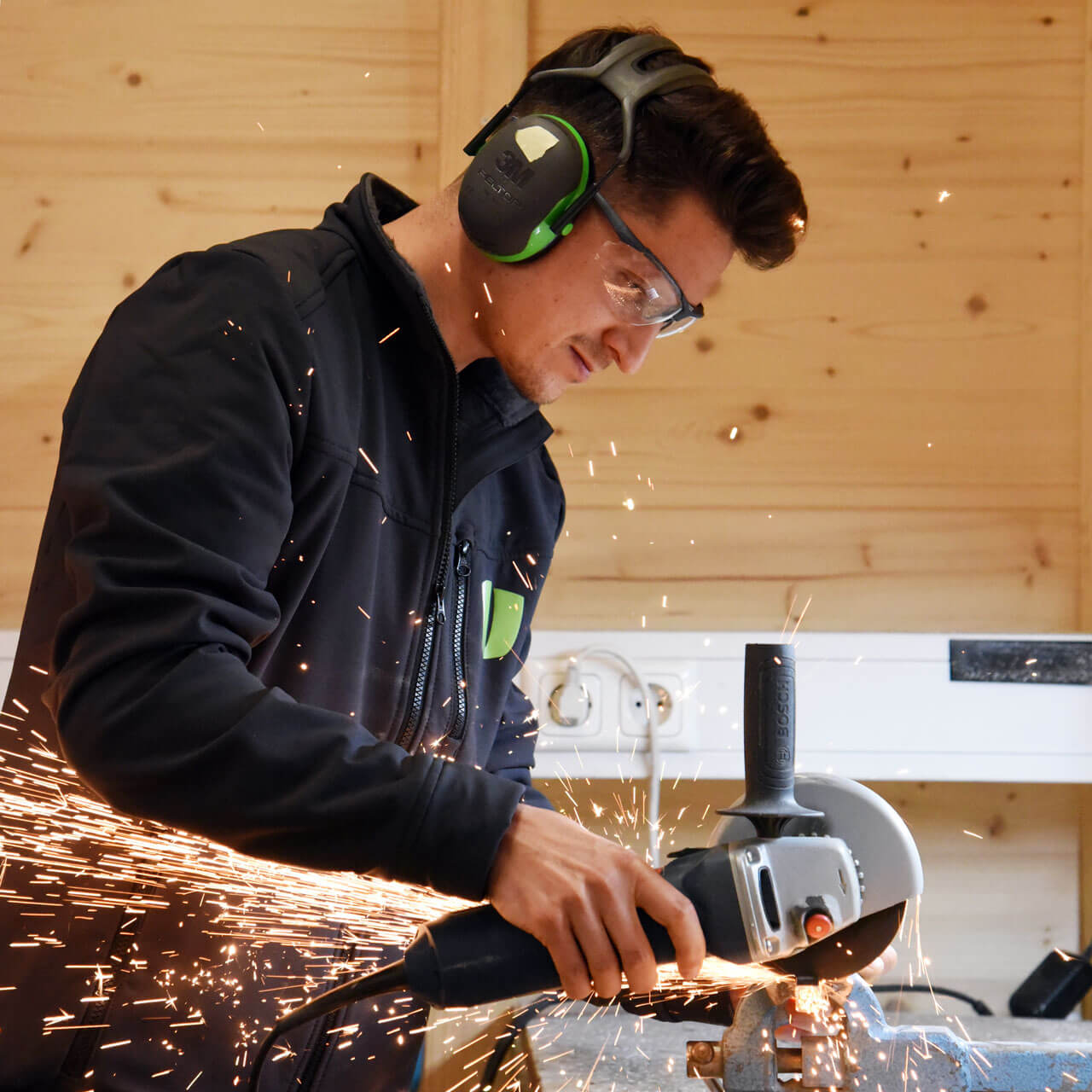 Ein Orthopädietechniker schleift in der Werkstatt und hat Schallschutz-Kopfhörer auf.